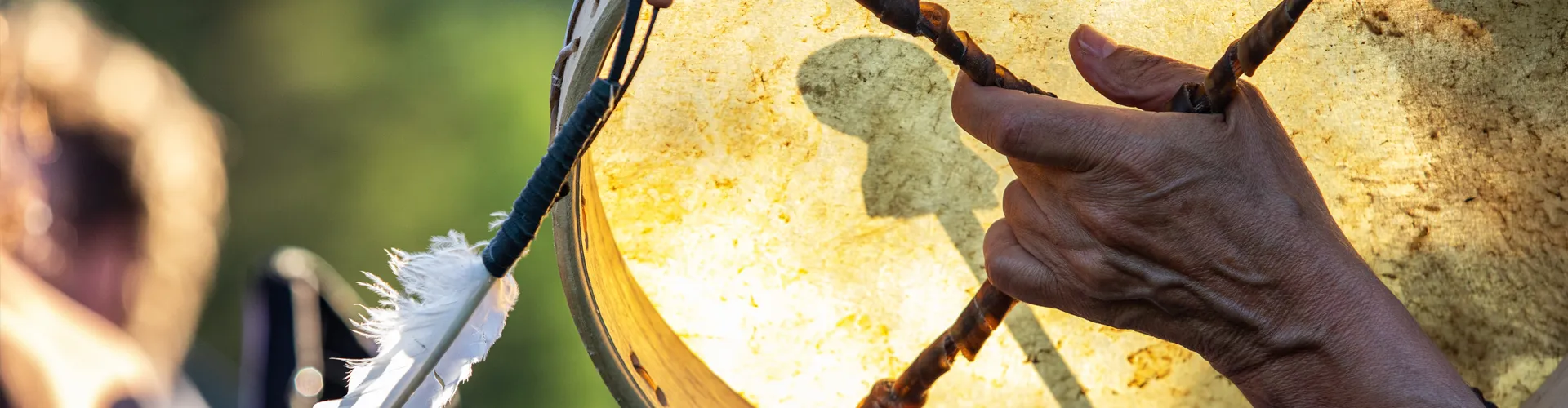 A close-up photo of a hand using a ceremonial drum with feathers on it.