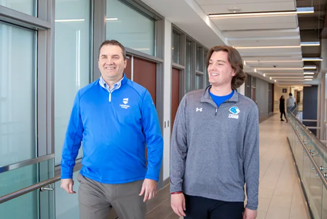 Rob Kardas walking down a campus hallway with student.