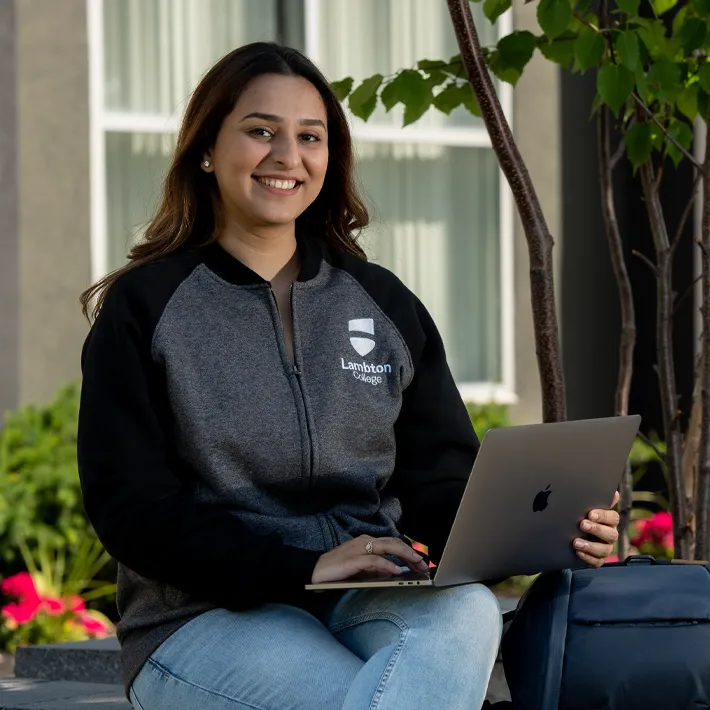 An international student sitting outside with a laptop smiling for a photo.