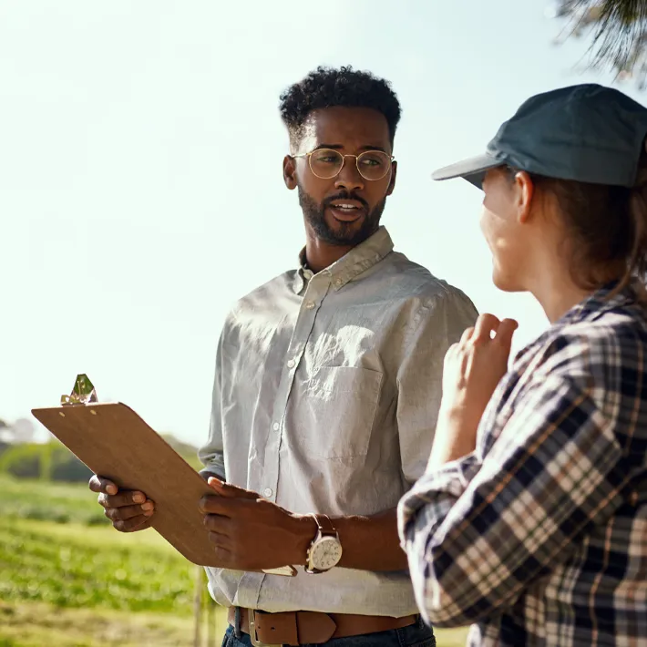 A man and a woman in a field holding clipboard and ipad.