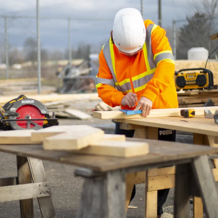 A student at a saw table measuring wood at a construction site.
