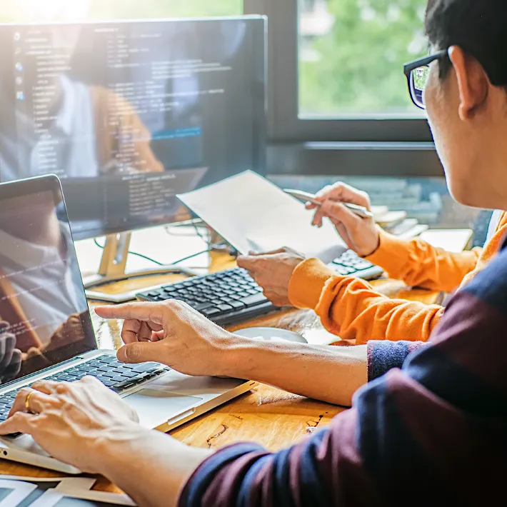 Two people researching and reviewing data on screen.