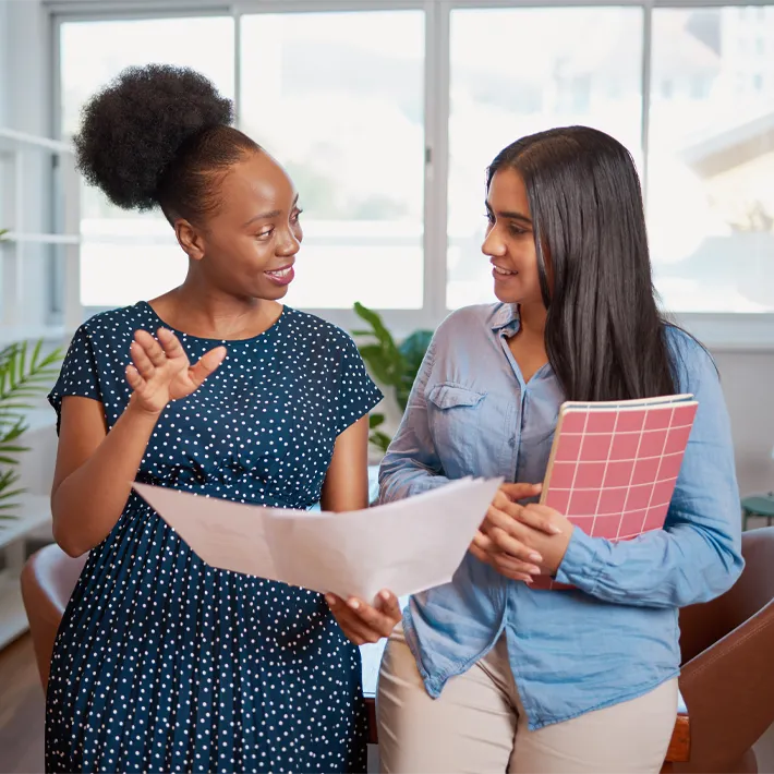 A photo of an adult mentor talking with a student while holding sheets of paper and notebooks.