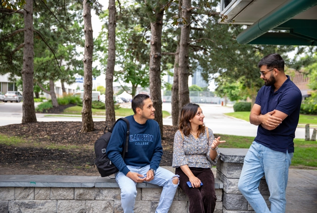 Students sitting outside and talking with trees and a road in the background.