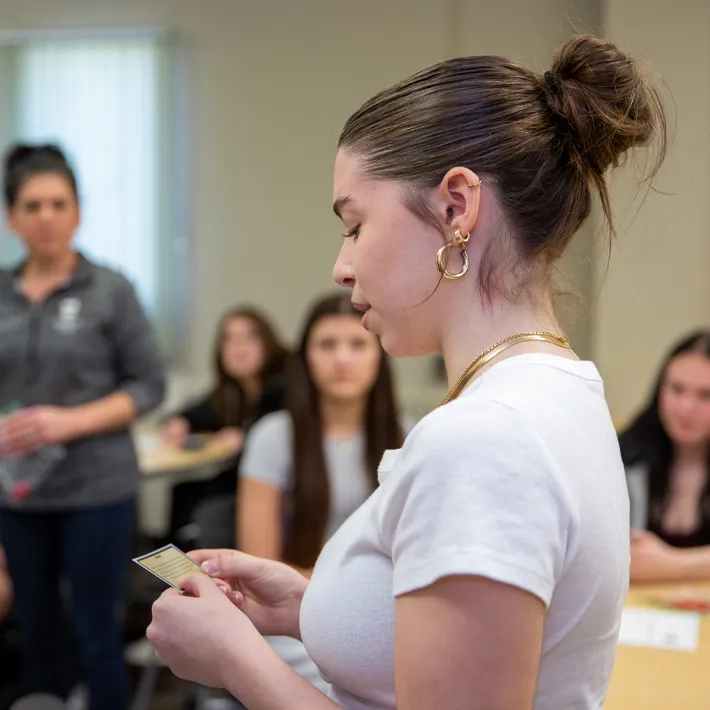 Dual credit student standing in a full classroom reading off notes to classmates.