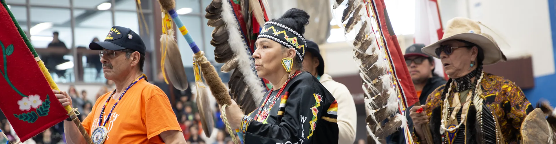 A group of indigenous peoples in a pow wow ceremony holding poles.