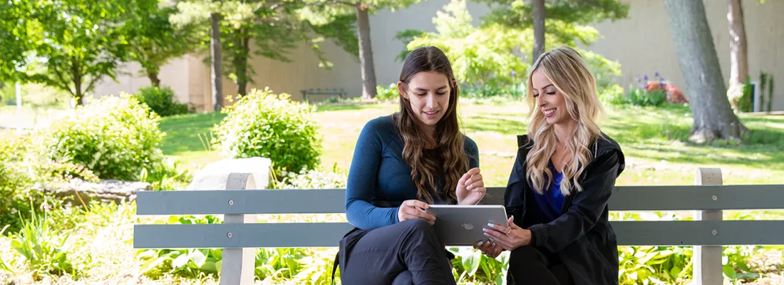A recruitment member and a student looking at ipad outside sitting on a bench.