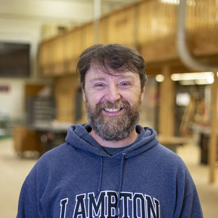 A photo of a carpenter student posing for photo in wood shop.