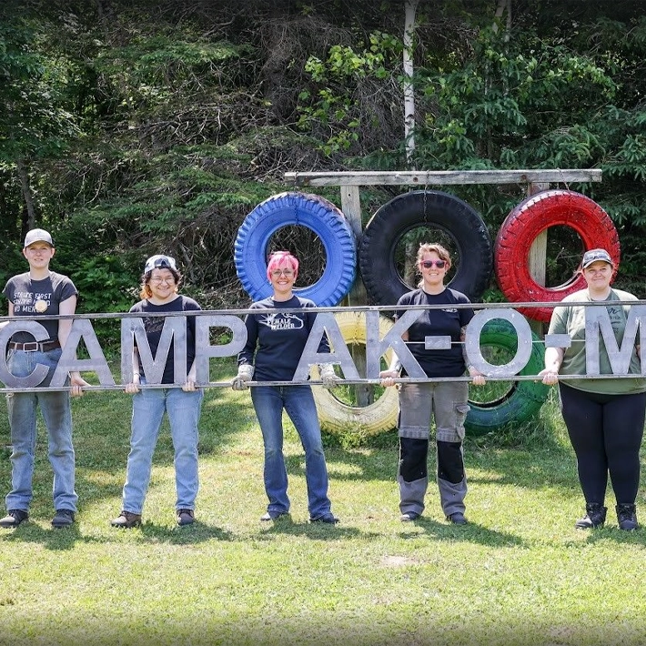 Women standing from a sign posing for photo outside.