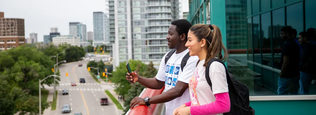 A photo of two students on the campus balcony area overlooking the city of Toronto.