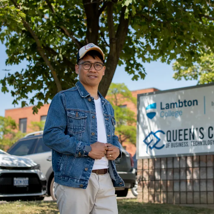 An international student posing for a photo outside of campus sign.