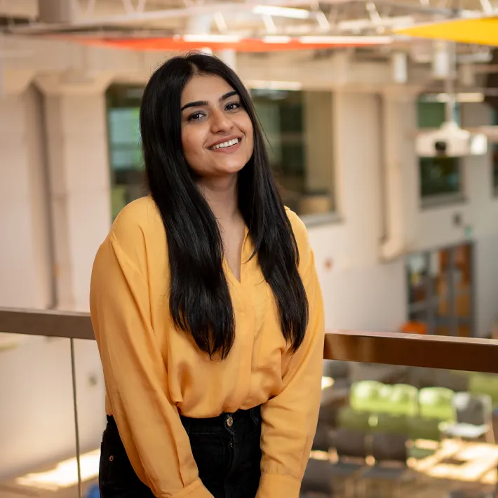 An international student posing for photo on campus wearing yellow shirt.