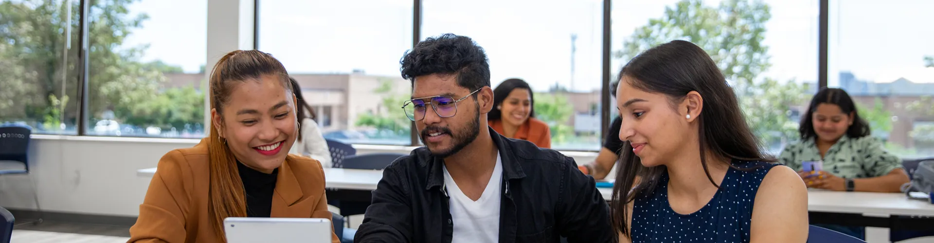 A photo of students sitting in a classroom looking at ipad with windows behind them.