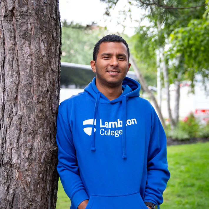 A toronto international student wearing blue lambton college hoodie posing for photo outside.