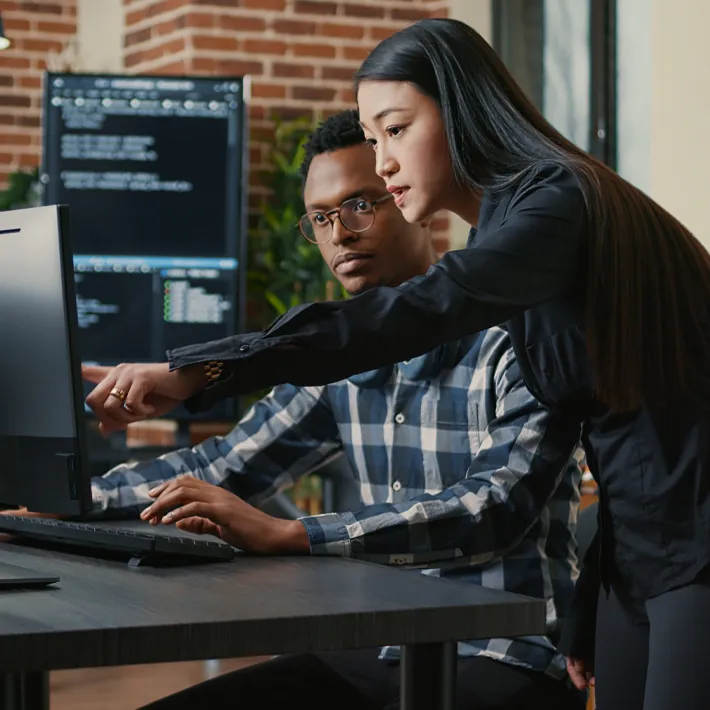 Two programmers looking reviewing code on programmer screen in office.