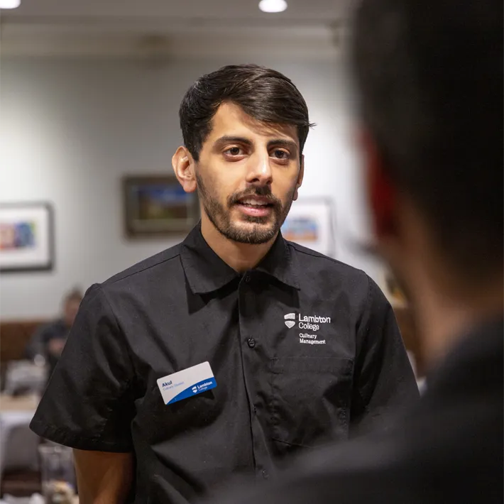 A student speaking to guest in Capstones restaurant.