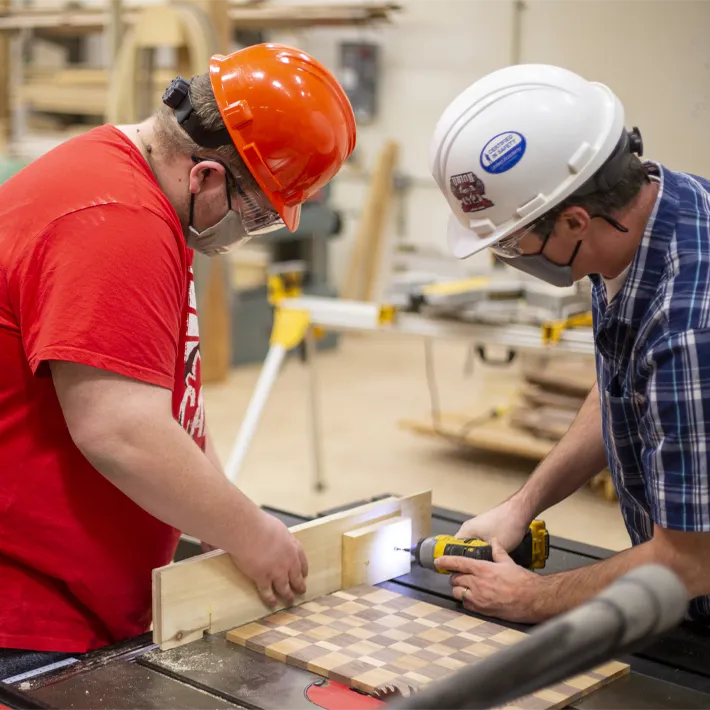 Students in shop using hand drill and weaing protective gear.