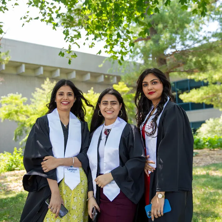 Three women international students posing for photo outside wearing convocation gowns.