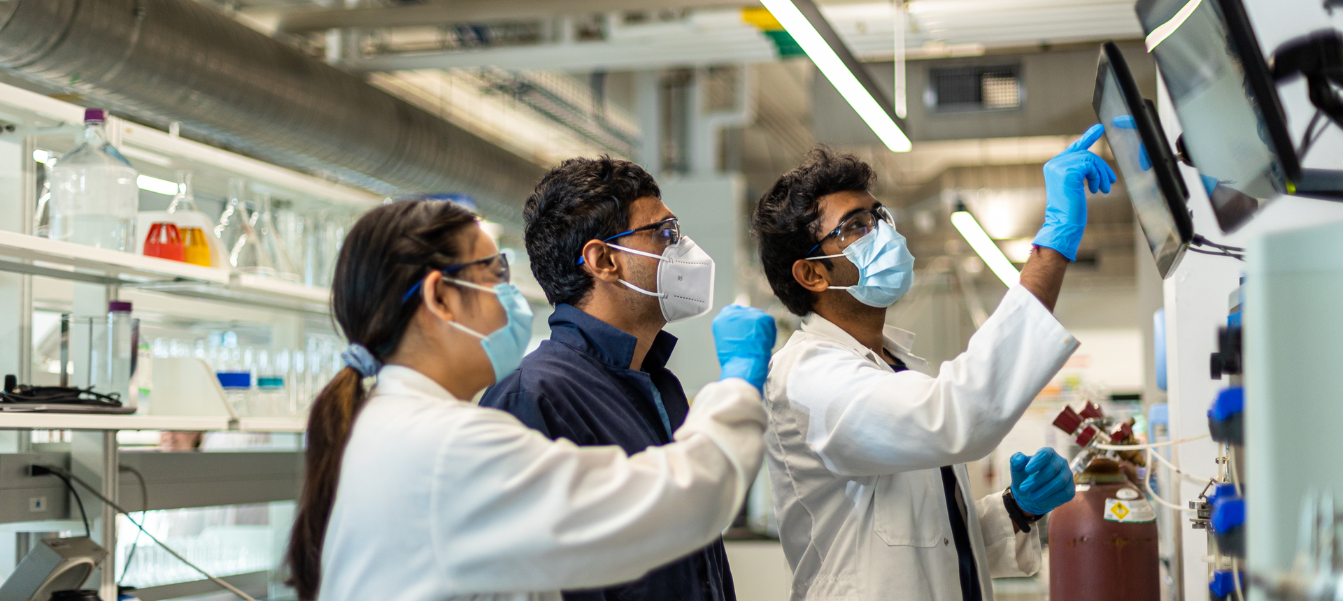 Three people in lab coats in a lab working on a computer